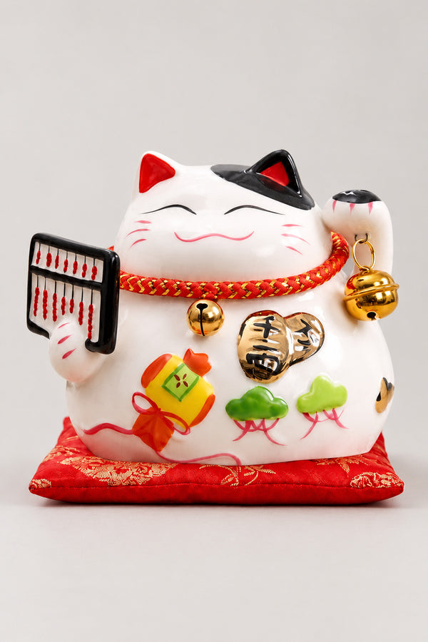 Abacus Maneki Neko Figurine 'Soroban' – calico ceramic lucky cat holding a black abacus, gold coin and fortune bag on the belly, Japanese maneki neko lucky cat figurine on a red brocade cushion, studio view