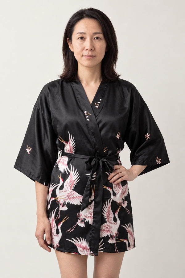 Black Crane Kimono Nightdress 'Yoizuru' – black women's short satin-look kimono nightdress with pink crane print and tie belt, Japanese robe, front view on model