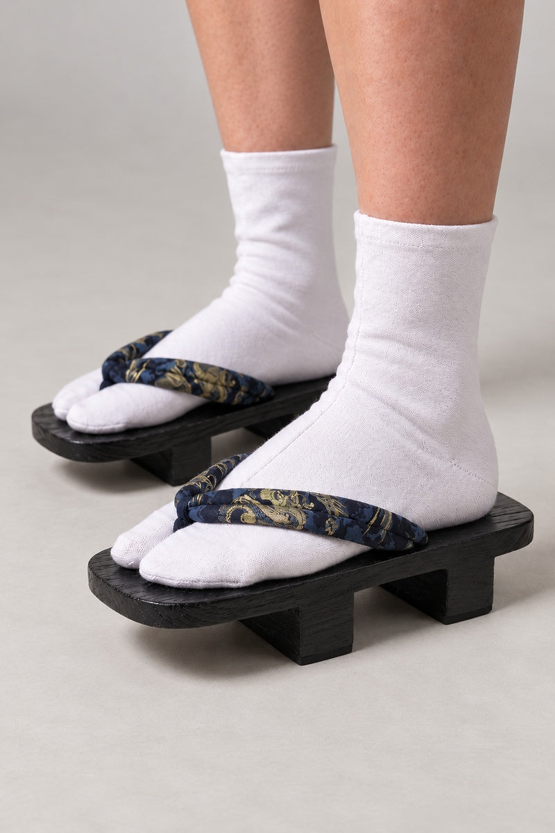 Black Dragon Geta 'Kinryuba' – black wooden geta with navy strap printed in gold and blue dragon, two-tooth wooden geta sandals with padded fabric strap, traditional Japanese footwear, worn with white tabi sock, side view on model