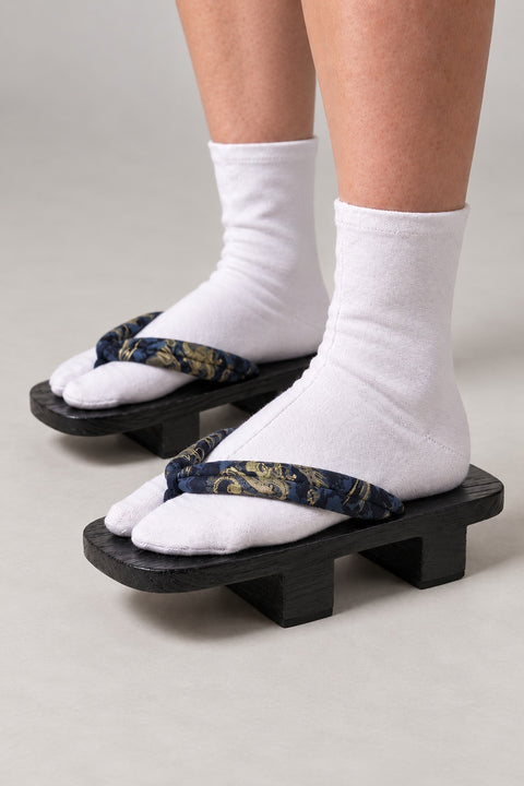 Black Dragon Geta 'Kinryuba' – black wooden geta with navy strap printed in gold and blue dragon, two-tooth wooden geta sandals with padded fabric strap, traditional Japanese footwear, worn with white tabi sock, side view on model