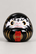 Black Shadow Daruma 'Kagemi' – black glossy ceramic daruma doll with both eyes painted, gold streaks and red kanji for opening luck on the belly, Japanese good luck doll, studio view
