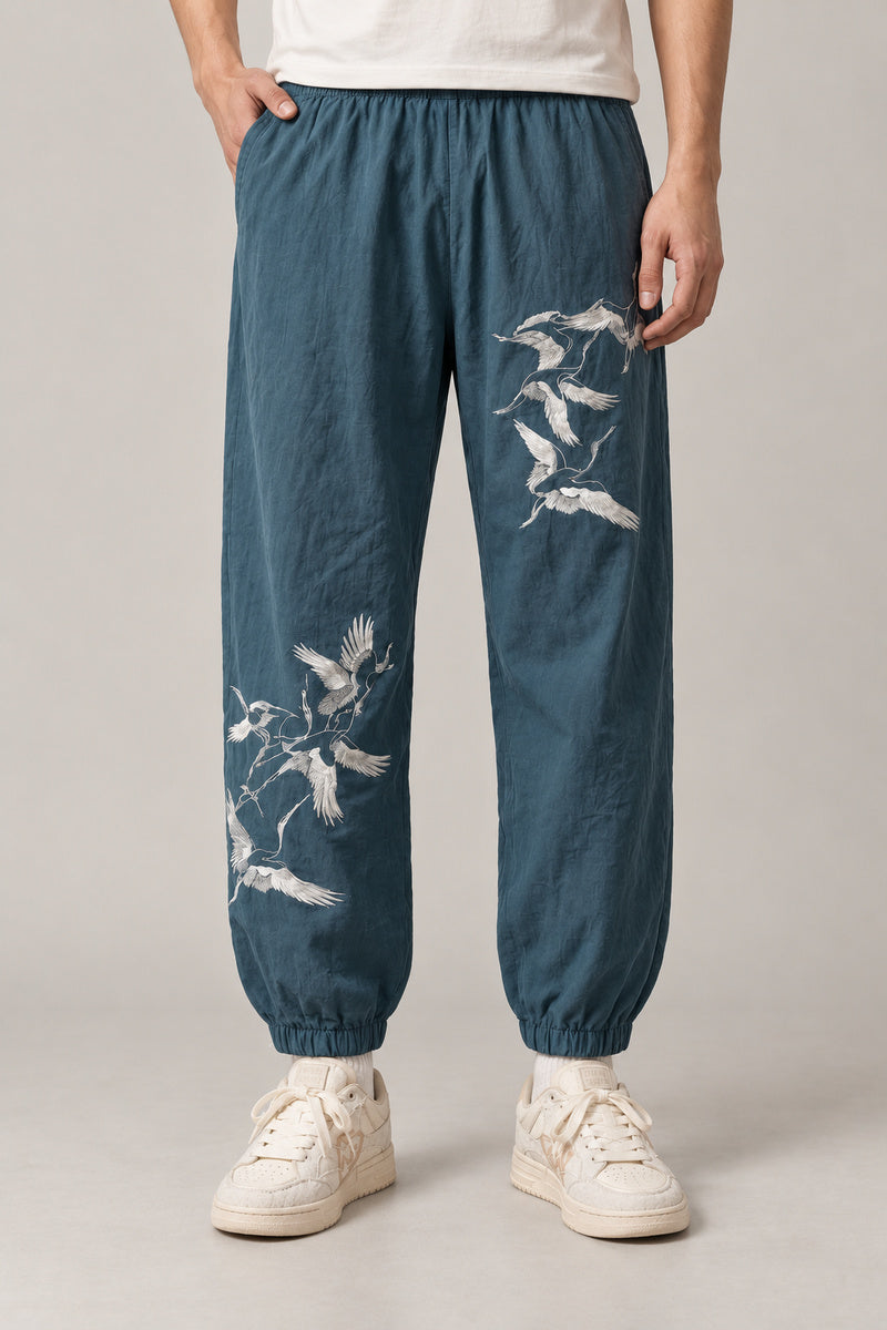 Crane Flock Embroidered Pants 'Tsurumure' – teal joggers with embroidered flock of white cranes, Japanese streetwear pants, front view on model