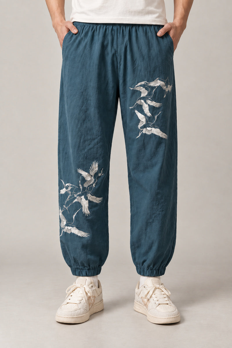 Crane Flock Embroidered Pants 'Tsurumure' – teal crane embroidered joggers, side view on model