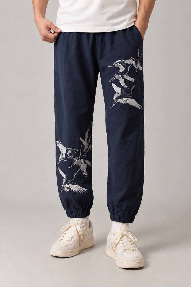 Crane Flock Embroidered Pants 'Tsurumure' – navy version of the crane flock embroidered joggers, front view on model