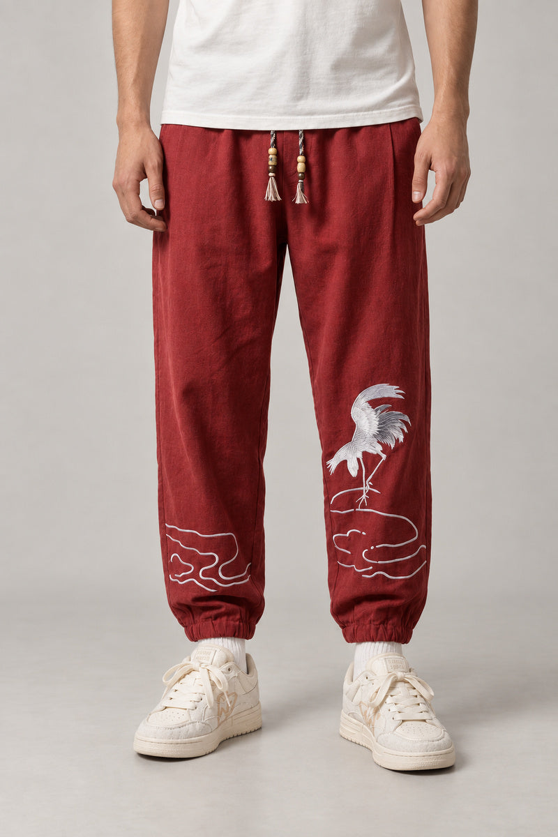 Dancing Crane Jogger Pants 'Sennen' – burgundy joggers with embroidered dancing crane and tassel drawstring, Japanese streetwear pants, front view on model