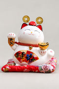 Great Fortune Plaque Lucky Cat 'Daikichi' – white ceramic lucky cat with gold coin headdress, gold ingot and red fan, Japanese maneki neko lucky cat figurine on a red brocade cushion, studio view