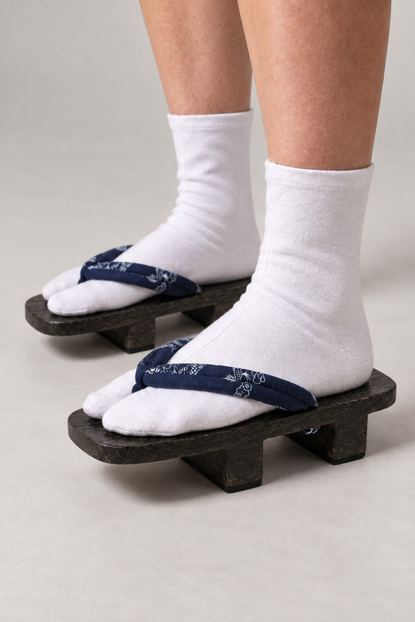 Indigo Crane Geta Clogs 'Aizuru' – dark wooden geta with navy strap printed in white cranes and blossom, two-tooth wooden geta sandals with padded fabric strap, traditional Japanese footwear, worn with white tabi sock, side view on model
