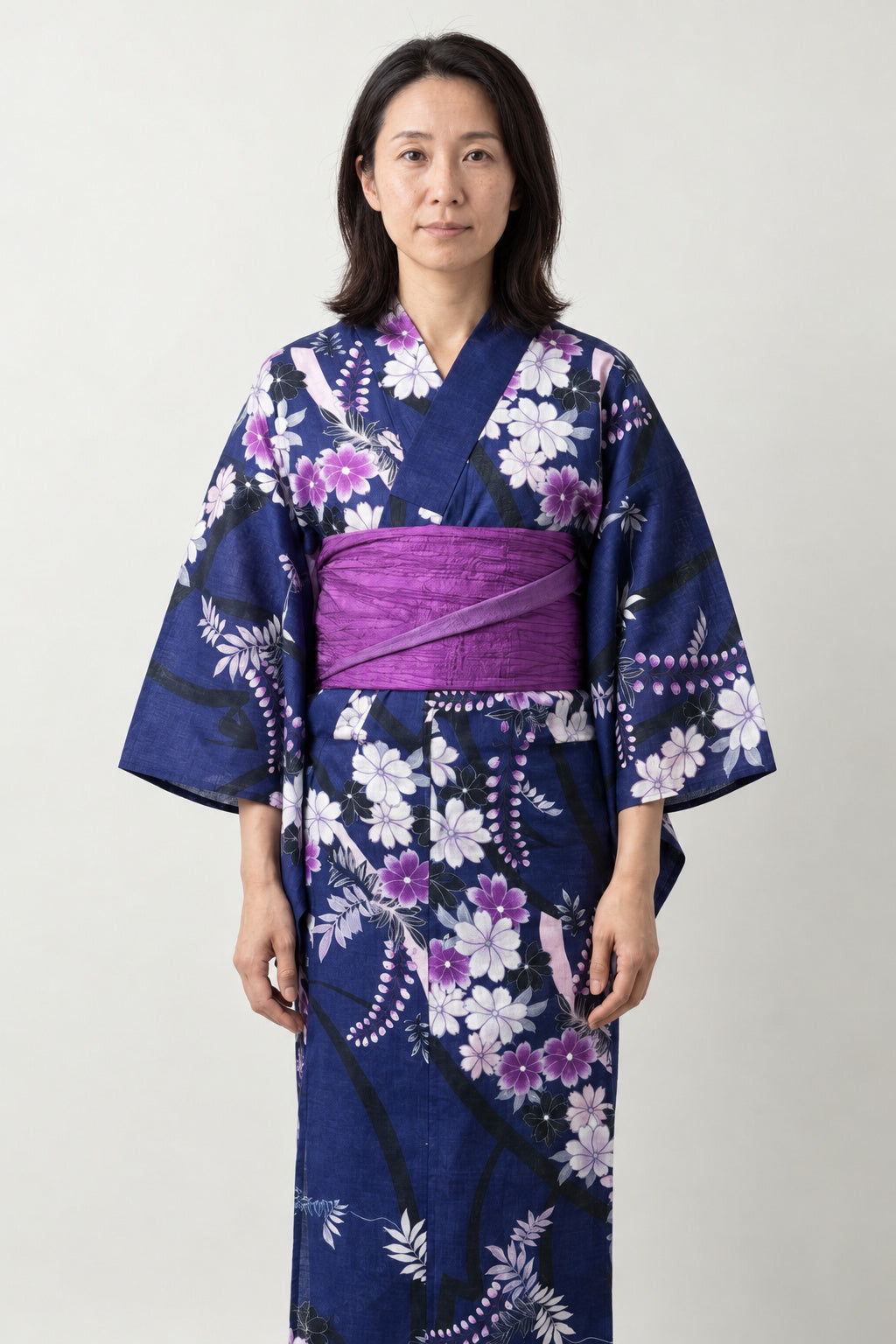 Indigo Wisteria Kimono Robe 'Fujidana' – indigo women's kimono robe with white wisteria and floral print and purple obi belt, traditional Japanese yukata, front view on model