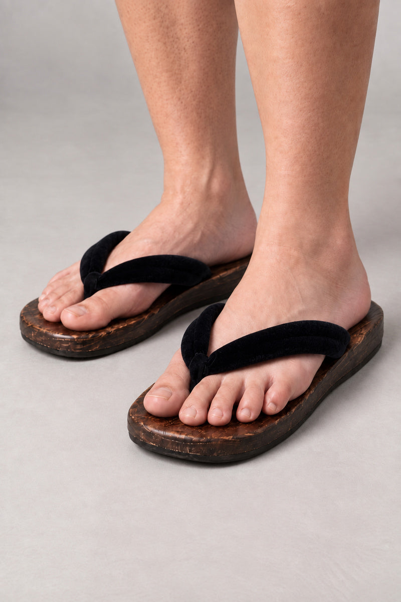 Japanese Flip Flops 'Karakoro' – wooden flip flops with plain black padded thong, flat Japanese wooden sandals worn barefoot, front view on model
