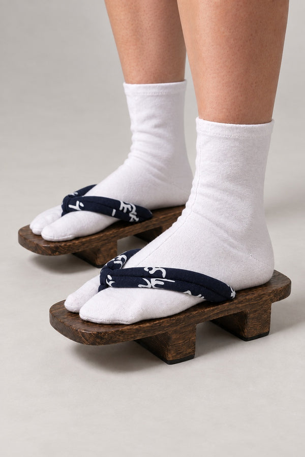 Japanese Geta Sandals 'Kotoba' – brown wooden geta with navy strap printed in white brushed kanji, two-tooth wooden geta sandals with padded fabric strap, traditional Japanese footwear, worn with white tabi sock, side view on model