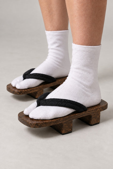Japanese Wooden Geta Sandals 'Tsunahana' – brown wooden geta with black corded strap, classic two-tooth wooden geta sandals with padded fabric strap, traditional Japanese footwear, worn with white tabi sock, side view on model
