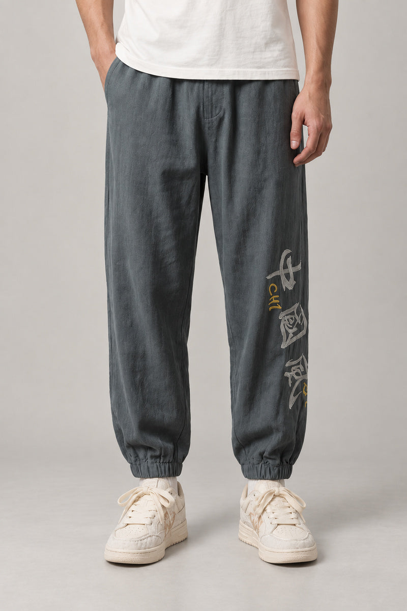 Kanji Calligraphy Jogger Pants 'Fude' – grey joggers with kanji calligraphy print on the leg, Japanese streetwear pants, front view on model