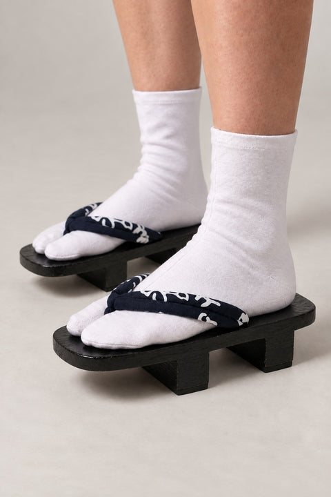 Kanji Geta Shoes 'Sumimoji' – black wooden geta with navy strap printed in white brushed kanji, two-tooth wooden geta sandals with padded fabric strap, traditional Japanese footwear, worn with white tabi sock, side view on model