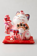 Large Pink Maneki Neko Statue 'Ooneko' – large ceramic lucky cat statue in a painted pink kimono with red bow holding a fan and bell charm, Japanese maneki neko lucky cat figurine on a red brocade cushion, studio view