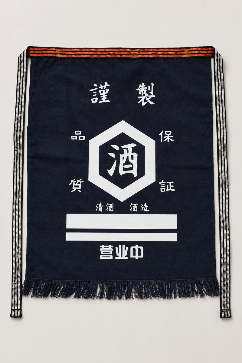 Maekake – indigo maekake apron printed with a round sake crest and quality seal, traditional Japanese sake brewery waist apron with fringed hem, studio view