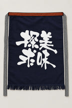 Maekake – indigo maekake apron printed with two bold brushed kanji for delicious, traditional Japanese sake brewery waist apron with fringed hem, studio view
