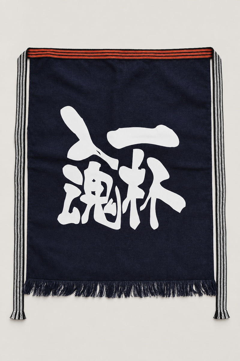 Maekake – indigo maekake apron printed with the kanji for one cup and spirit, traditional Japanese sake brewery waist apron with fringed hem, studio view