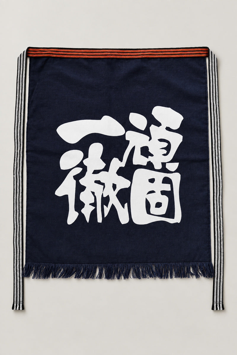 Maekake – indigo maekake apron printed with the kanji for steadfast and thorough, traditional Japanese sake brewery waist apron with fringed hem, studio view