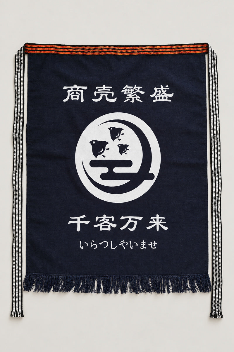 Maekake – indigo maekake apron printed with a fish crest and the kanji for prosperous business, traditional Japanese sake brewery waist apron with fringed hem, studio view