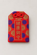 Omamori – red brocade omamori amulet with gold kanji for health and chrysanthemums, Japanese lucky charm, studio view