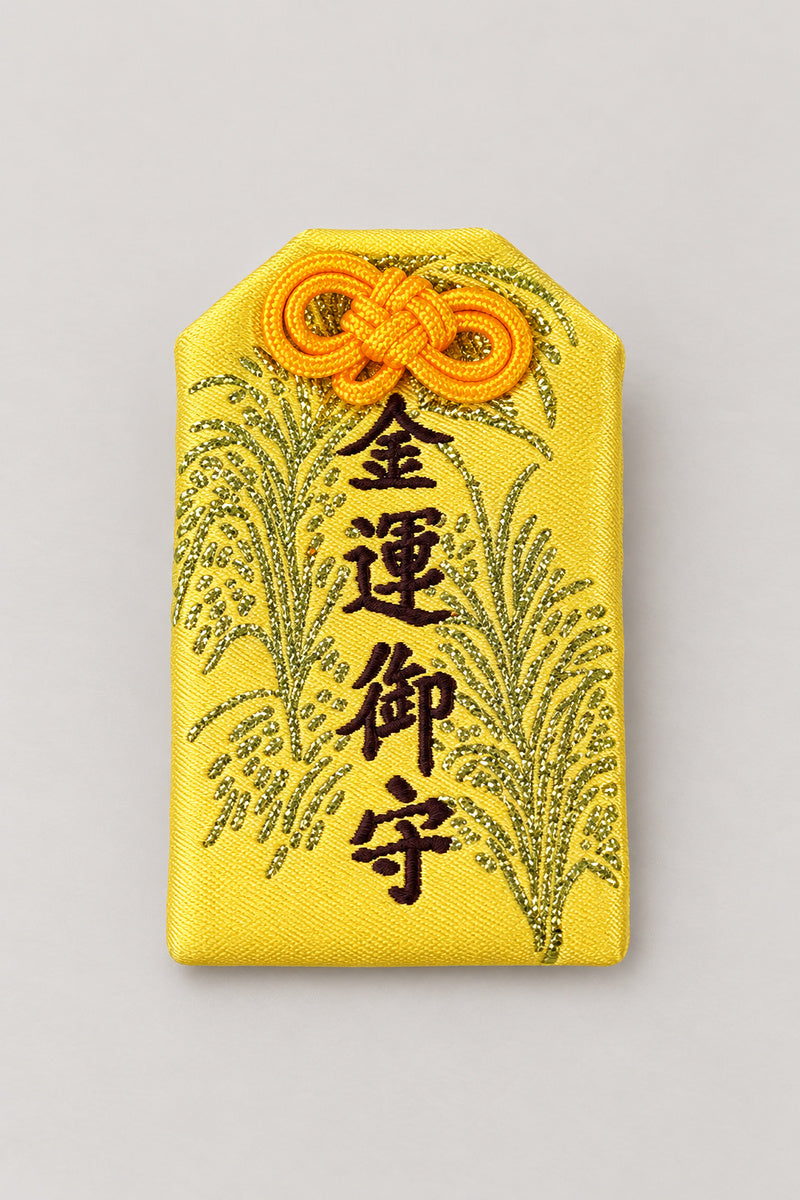Omamori – yellow brocade omamori amulet with gold kanji for money luck and rice ears, Japanese lucky charm, studio view