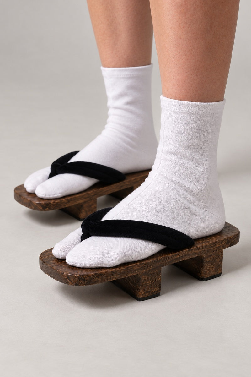 Plain Wooden Geta Shoes 'Kihon' – plain brown wooden geta with black strap, basic two-tooth wooden geta sandals with padded fabric strap, traditional Japanese footwear, worn with white tabi sock, side view on model