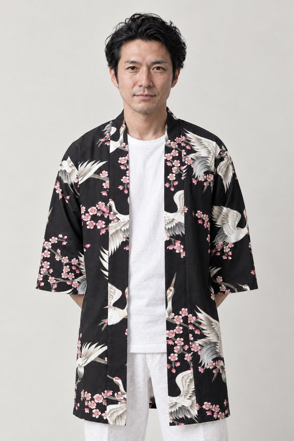 Sakura Crane Japanese Happi 'Harutsuru' – black happi coat with white cranes and pink cherry blossom print, Japanese happi coat, unisex festival jacket, front view on model
