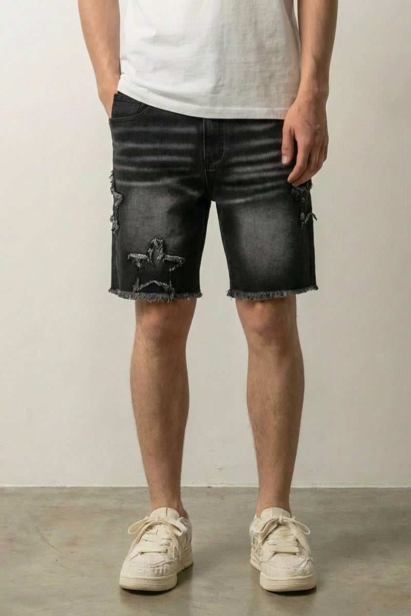 Star Print Black Denim Shorts 'Hoshikuzu' – black washed denim shorts with frayed star patches and raw hem, front view on model, studio