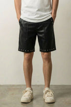 Studded Faux Leather Shorts 'Byo' – black studded faux leather shorts with silver studs at the hem, front view on model, studio