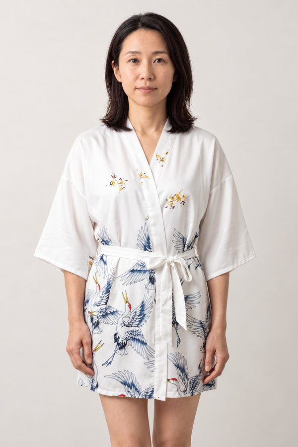 White Crane Short Satin Robe 'Yukizuru' – white women's short satin-look kimono robe with blue crane print and tie belt, Japanese dressing gown, front view on model