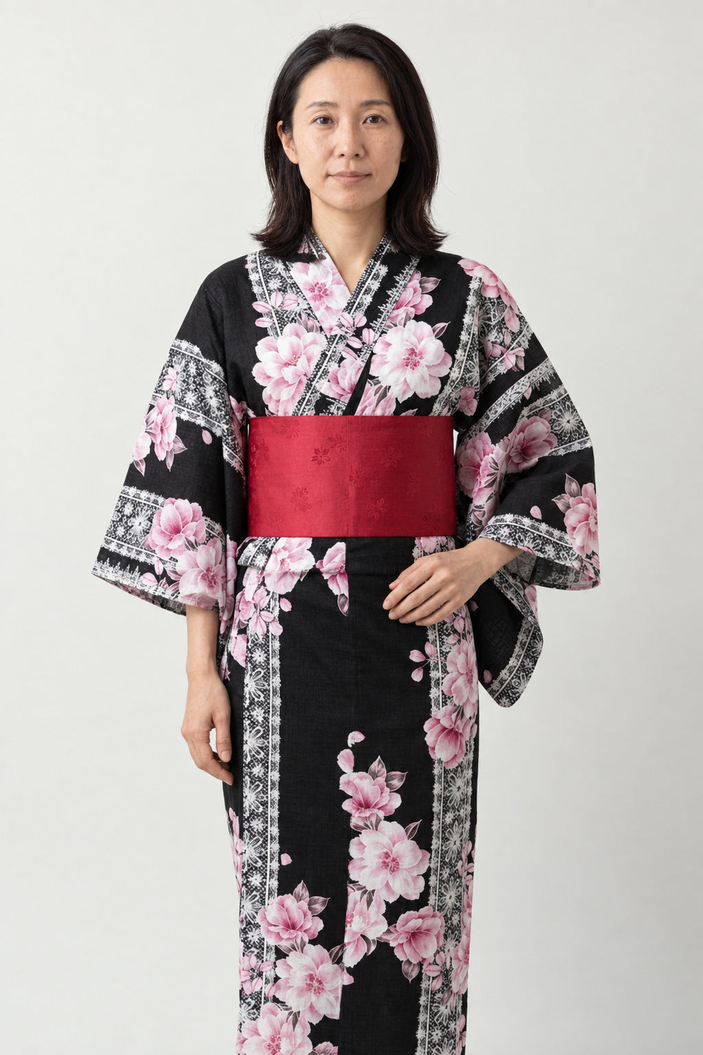 Women's Black Sakura Kimono 'Yaezakura' – black women's kimono with pink cherry blossom print and red obi belt, traditional Japanese yukata, front view on model