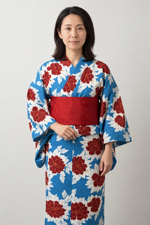 Women's Blue Peony Yukata 'Hibotan' – white women's yukata with blue and red peony print and red obi belt, traditional Japanese summer kimono, front view on model