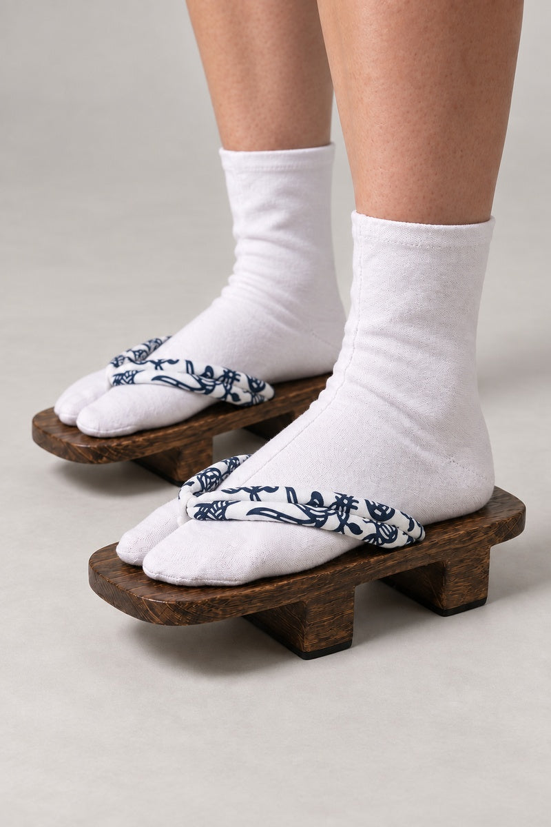 Women's Geta Sandals 'Shirahana' – brown wooden geta with white strap printed in navy fish and flowers, women's two-tooth wooden geta sandals with padded fabric strap, traditional Japanese footwear, worn with white tabi sock, side view on model